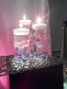 A collection of three cylinders with submerged orchids and floating candles.