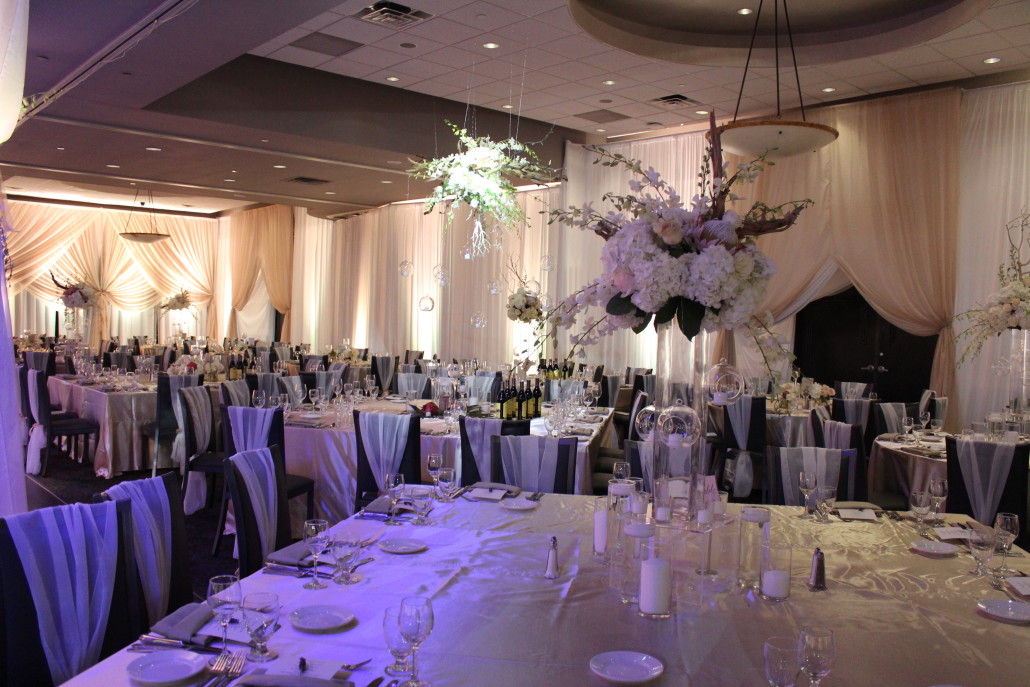The design featured three styles of centerpieces. One style was a hanging centerpiece made of drift wood and ghost wood branches, dripping with white orchids and glass globes. Other styles accented this focal look with similar flowers and candles.